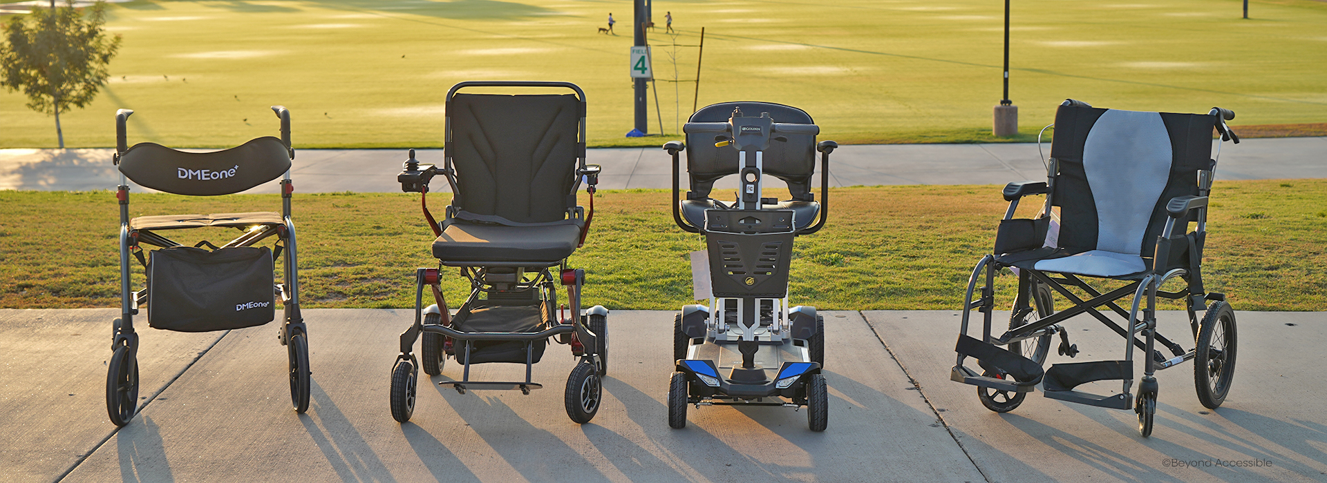 Photo of a rollator, powerchair, scooter, and transport chair on a sidewalk with a grass backdrop.