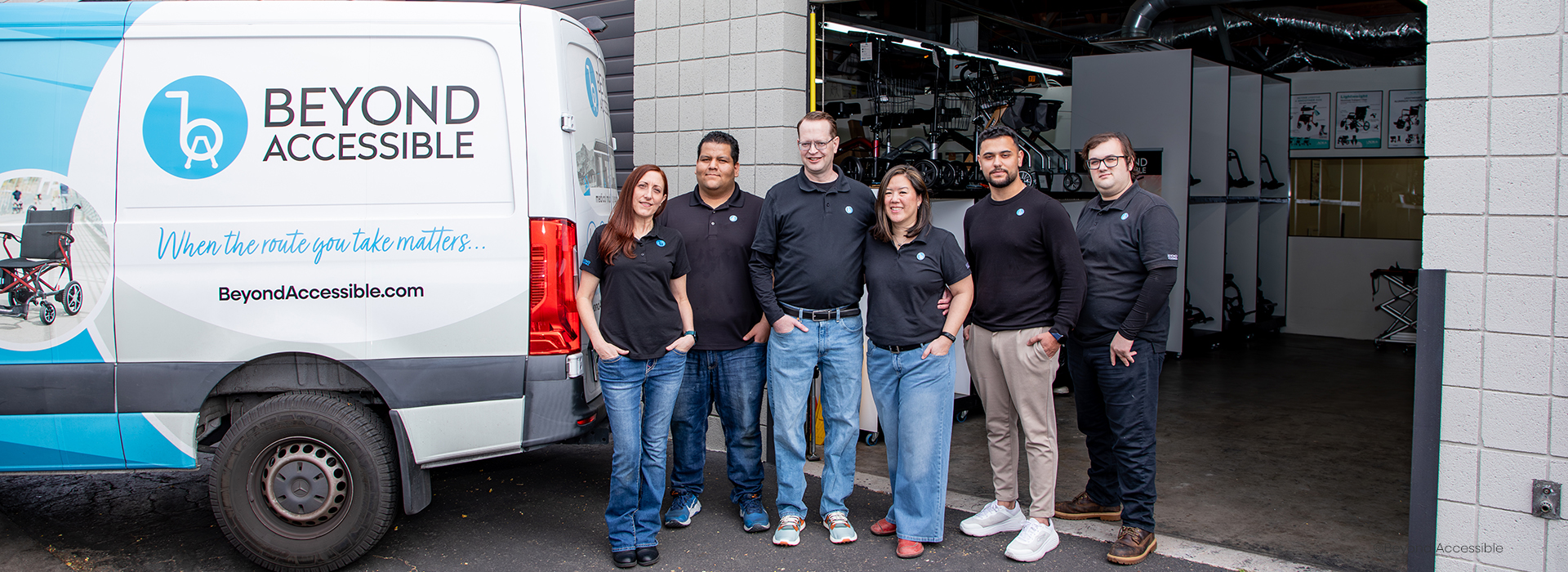 Photo of our team standing next to our work vehicle. Six people wearing black shirts standing in front of a open warehouse door.
