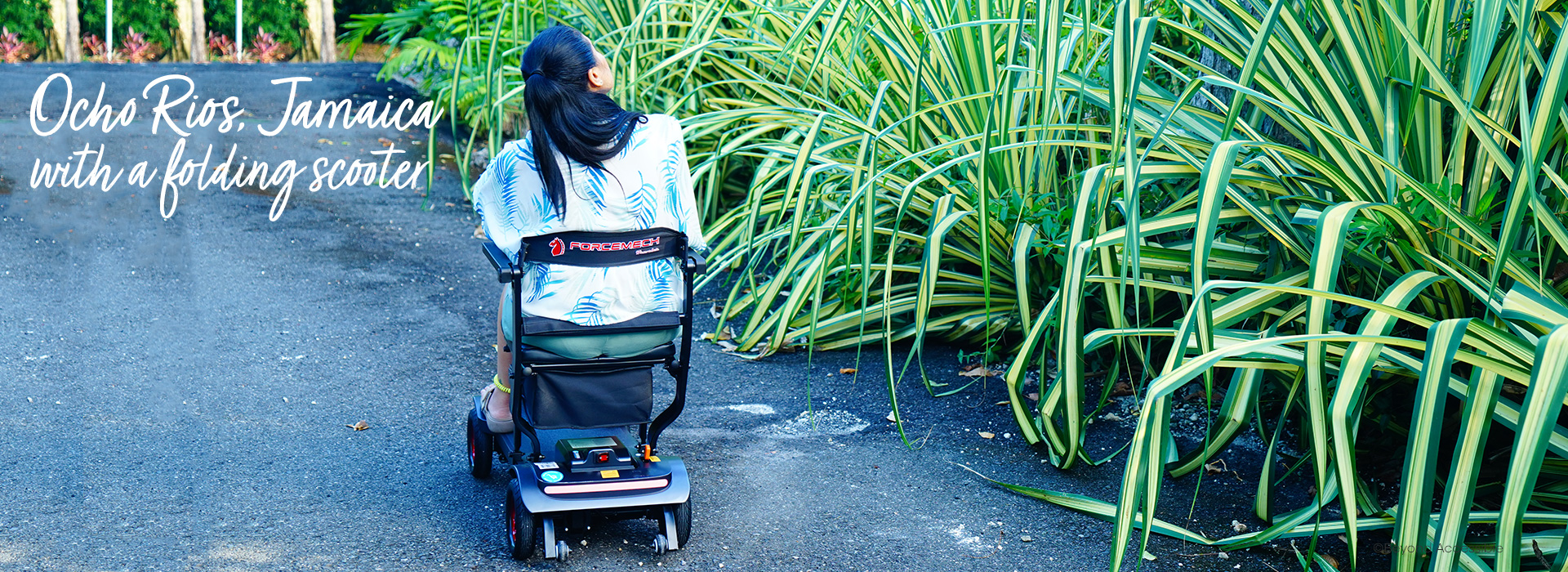 Woman on a travel folding scooter on a road next to some plants